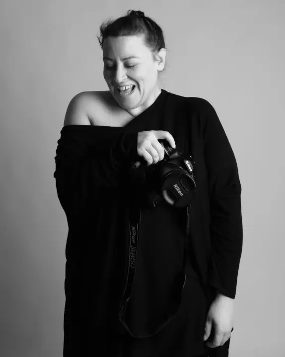 Photographe femme souriante tenant son appareil photo en studio – portrait naturel – Emilie Minary photographe portrait à Lyon